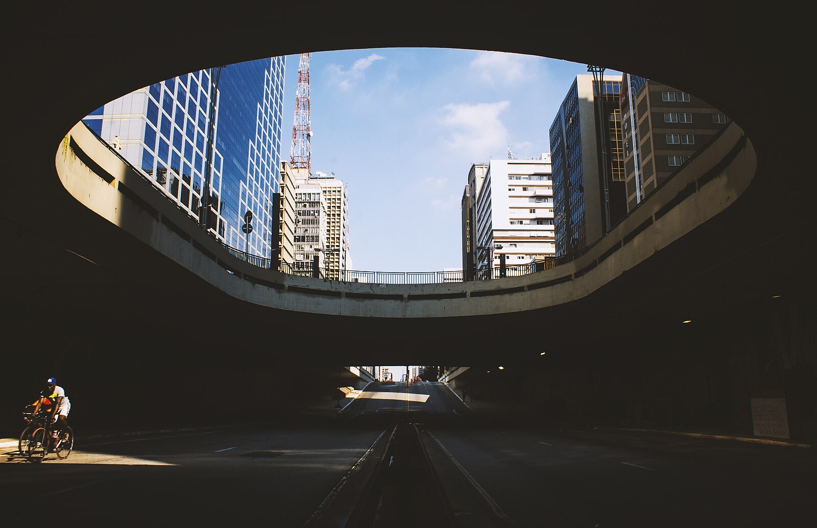 Avenida Paulista 由隧道的椭圆形洞口框入画面，前景有一名骑车人