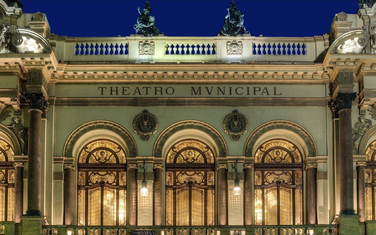 灯光照亮的 Theatro Municipal 正立面细部，可见拱券、立柱与建筑题字